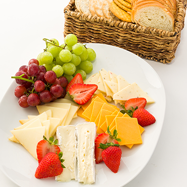 a plate of cheese and fruit alongside a basket of cracker options